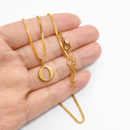 Gold necklace with a 'O' pendant held in a hand on a white background