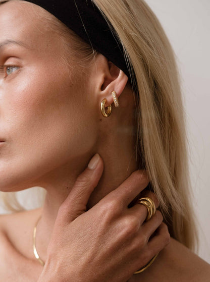 Close-up of a person wearing gold hoop earrings and rings, with a neutral background.