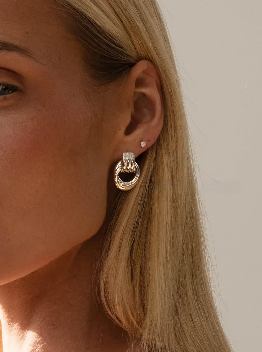 Close-up of a person wearing gold hoop earrings with a plain background