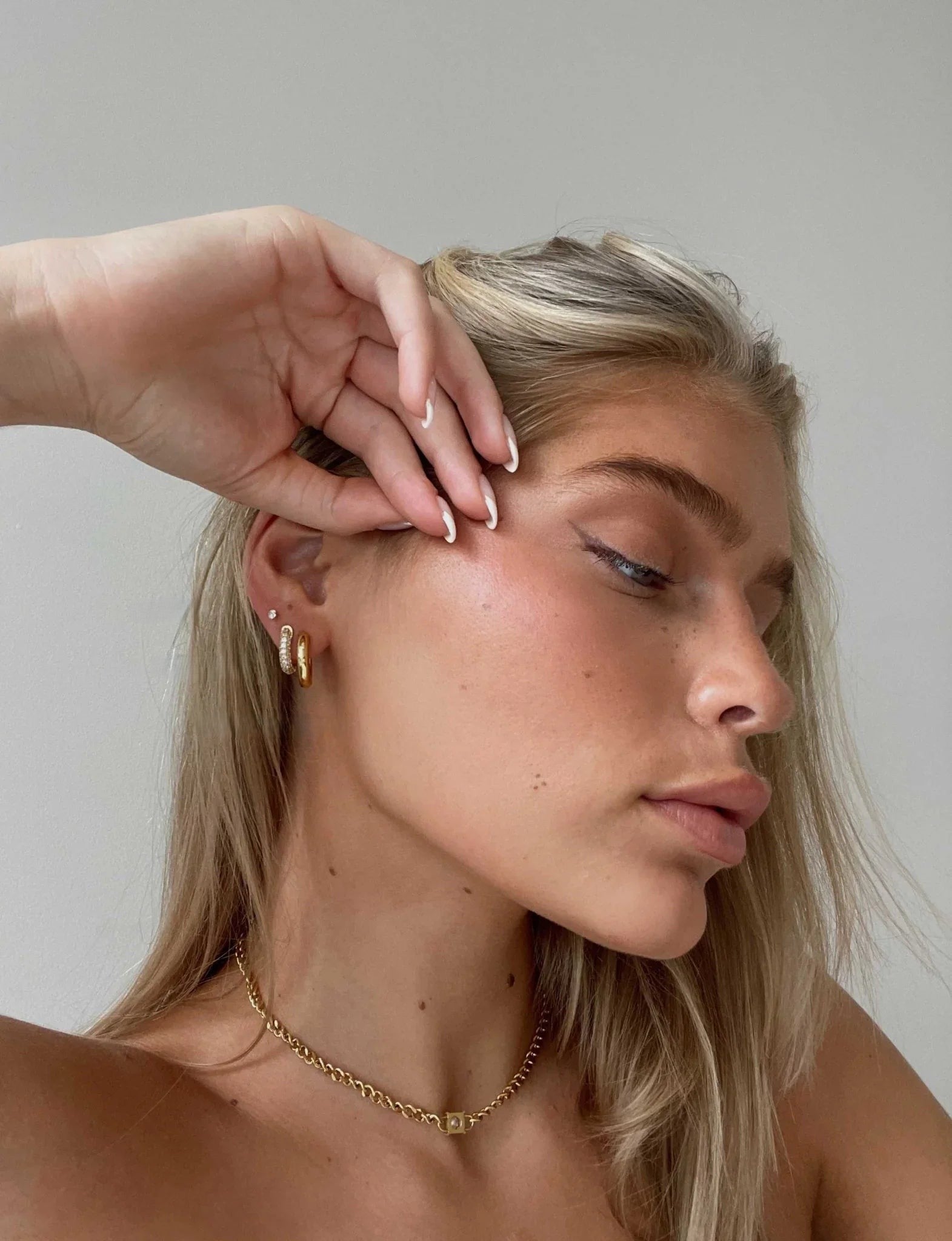 Woman with blonde hair and gold jewelry against a neutral background