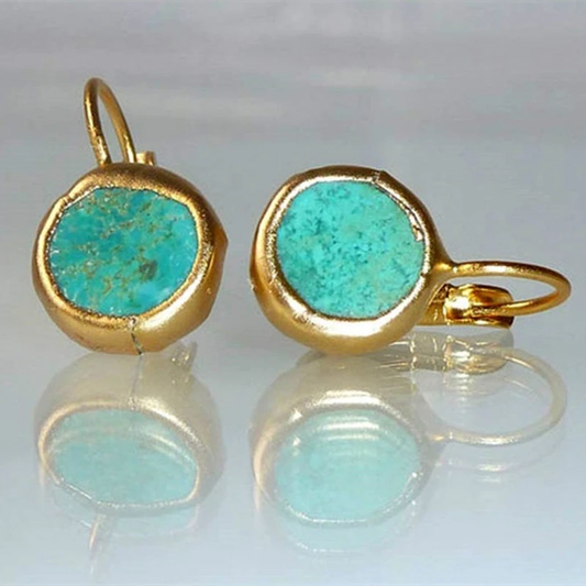 Gold turquoise earrings with round stones, reflecting on a glossy surface. Elegant jewelry, perfect for fashion accessories and gemstone enthusiasts.