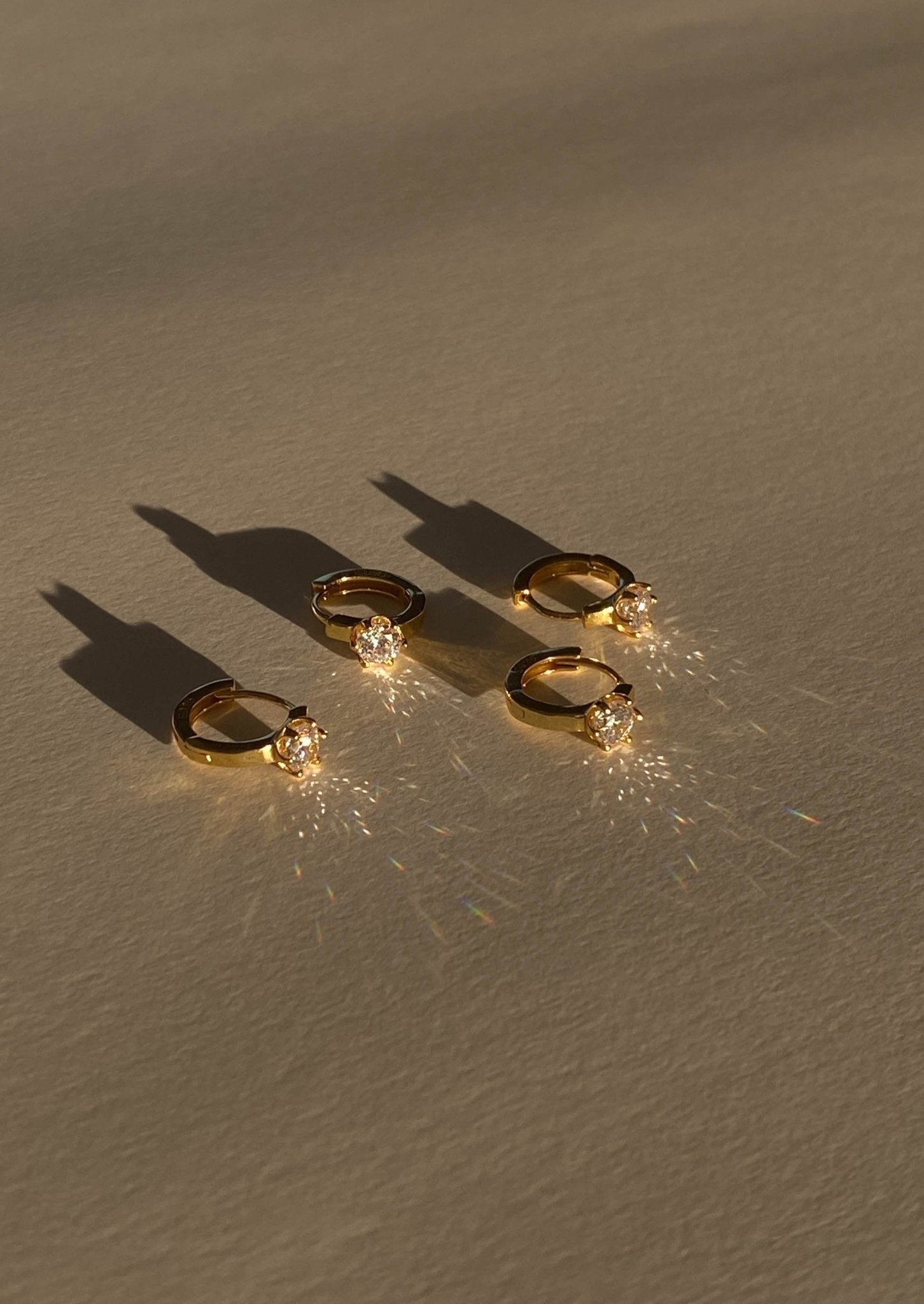 Four gold rings with sparkling diamonds casting shadows on a beige surface, showcasing luxury jewelry, elegance, and fine craftsmanship.