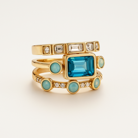Gold stackable rings with blue gemstones and clear crystals, featuring a large rectangular blue stone and circular turquoise accents. Elegant jewelry.