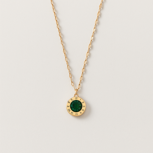Gold chain necklace with a round pendant featuring a green gemstone and Roman numerals. Elegant jewelry, minimalist design, fashion accessory.