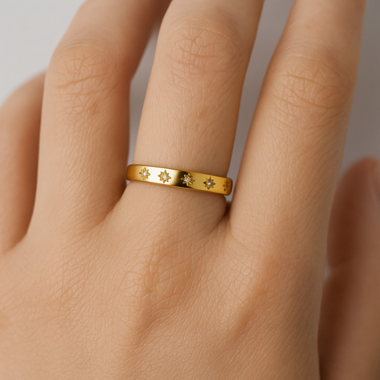 Gold ring with star designs on a person's finger against a neutral background