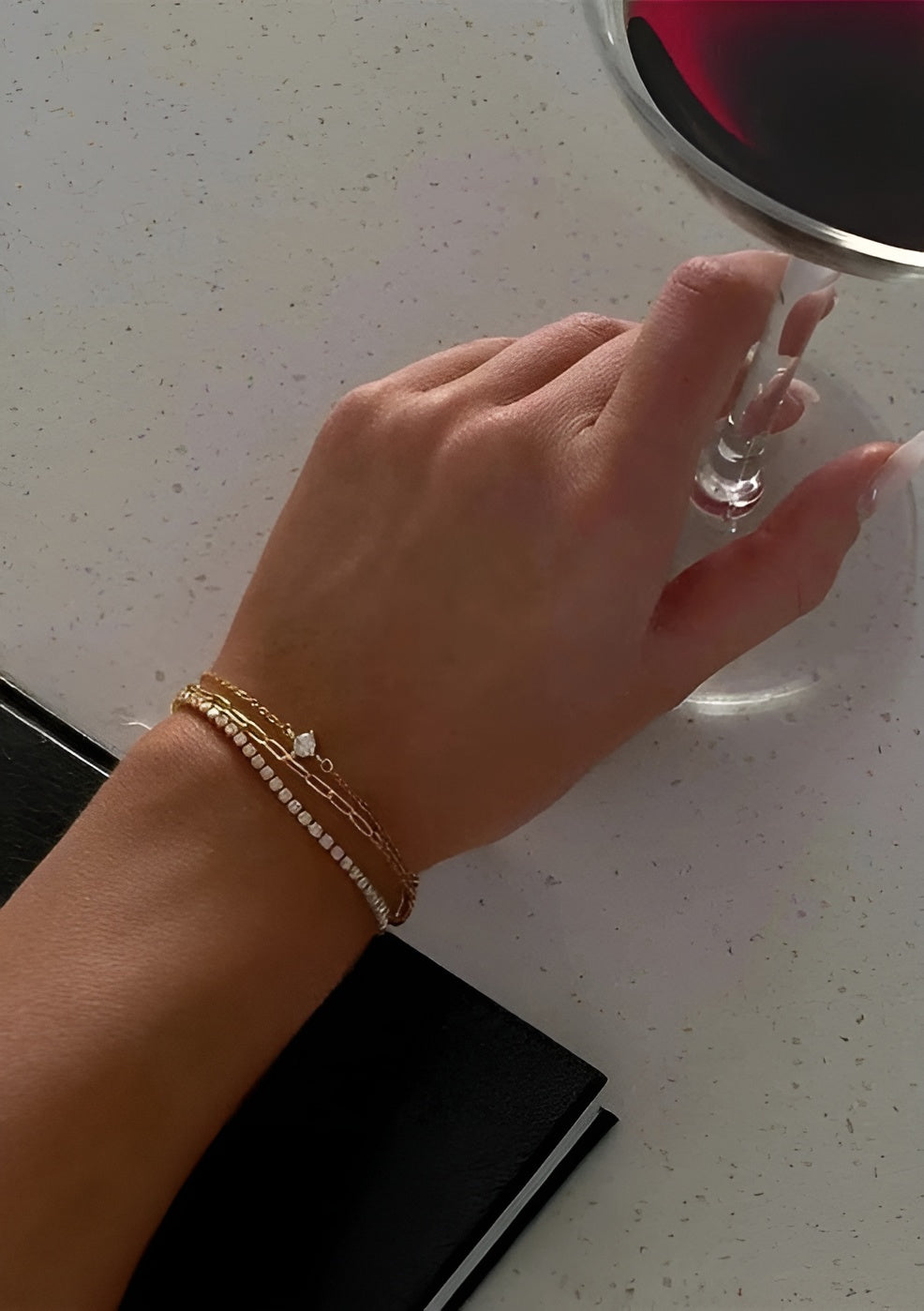 Hand with a bracelet holding a glass of red wine on a white surface