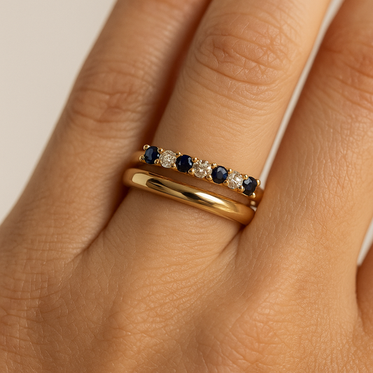 Gold ring with blue gemstones on a hand against a neutral background