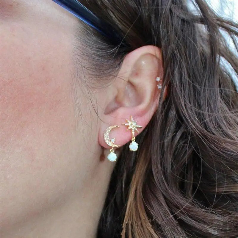 Woman wearing gold crescent moon and star earrings with dangling pearls, close-up. Trendy celestial jewelry, fashion accessory, ear piercing.