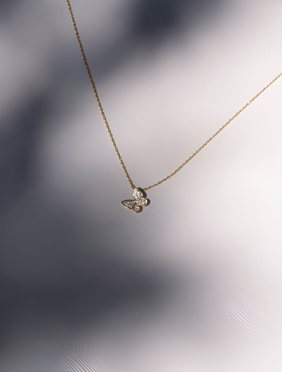 Gold butterfly necklace on a soft gray background