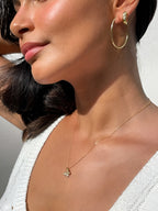 Close-up of a woman wearing gold hoop earrings and a delicate necklace with a pendant.