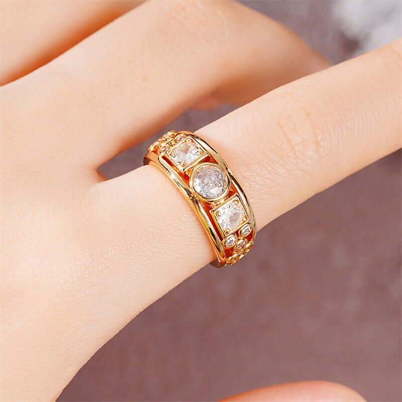 Gold ring with embedded stones on a person's finger against a neutral background