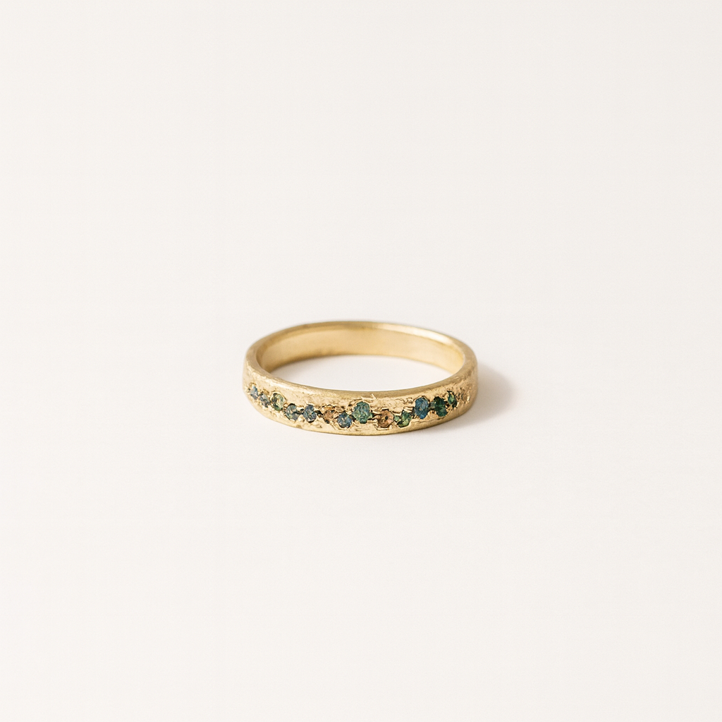 Gold ring with small green gemstones on a plain white background, elegant jewelry design, minimalist style, perfect for weddings or special occasions.