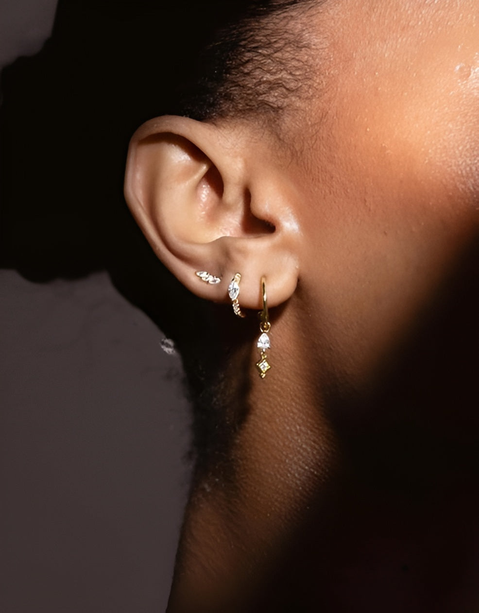 Close-up of an ear wearing gold hoop earrings with small diamonds against a dark background