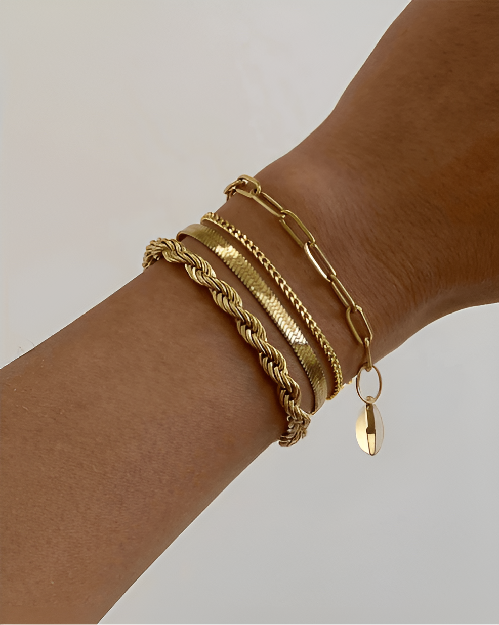 Gold bracelets on a wrist against a neutral background