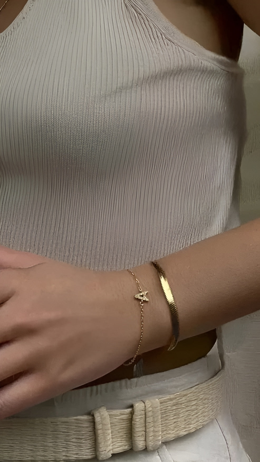 Close-up of a person wearing two gold bracelets on a neutral background