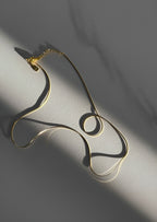 Gold necklace on a gray surface with soft shadows