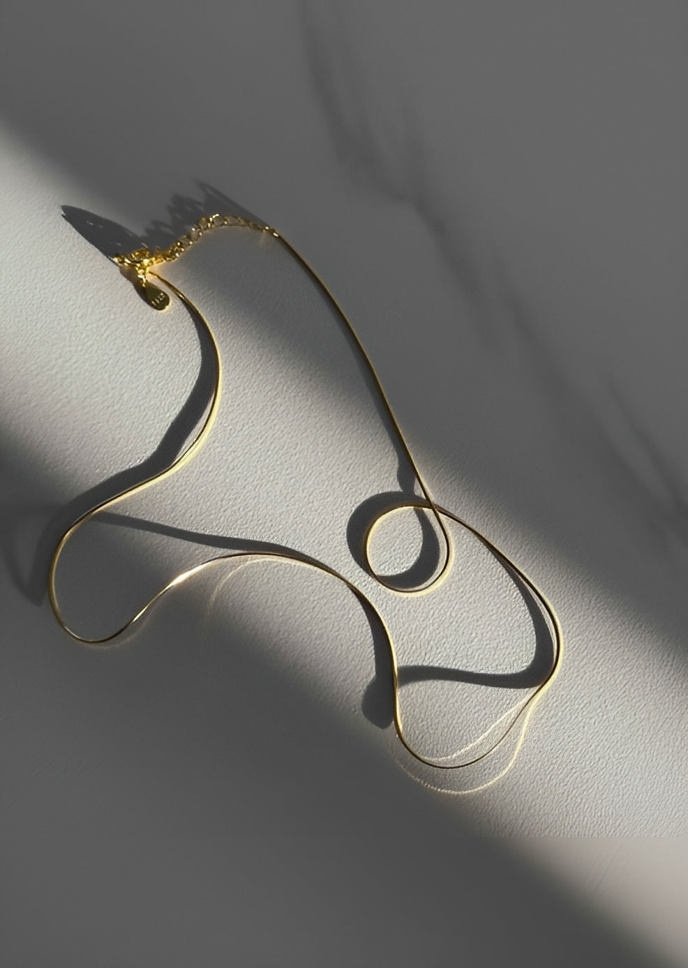 Gold necklace on a gray surface with soft shadows