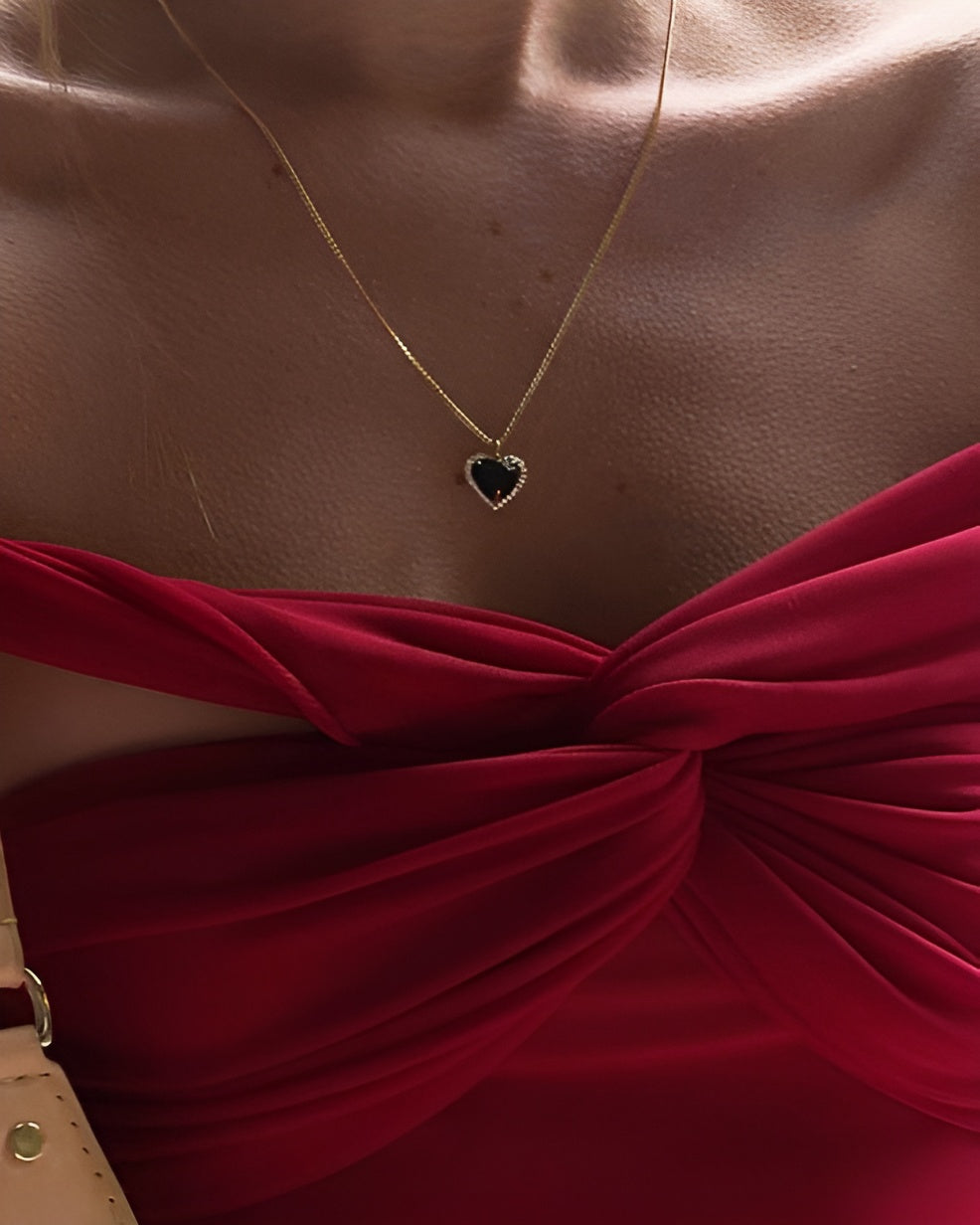 Heart-shaped necklace with green gemstone on a red top against a brown background
