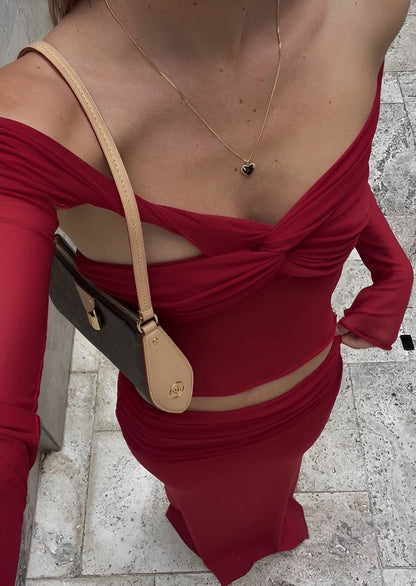 Person wearing a red off-shoulder top with cut-out design, holding a beige handbag.