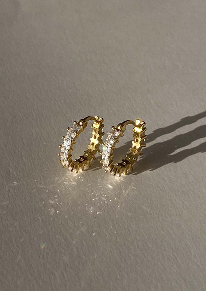 Gold hoop earrings with embedded stones on a gray background