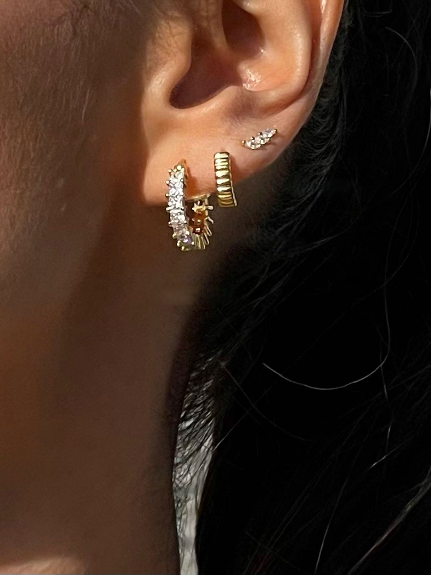 Close-up of an ear wearing gold hoop earrings with small diamonds.