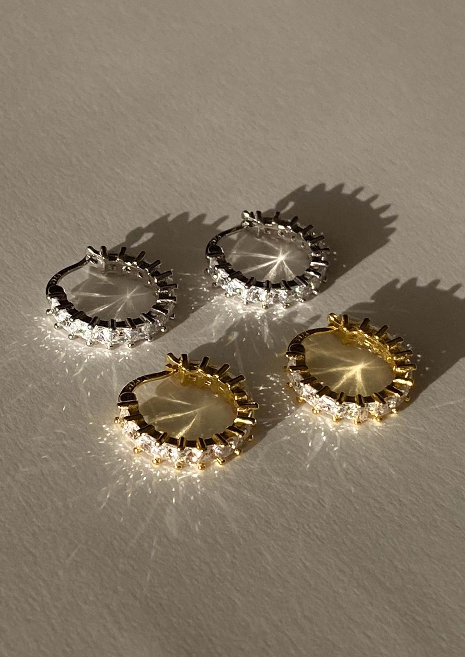 Four pairs of hoop earrings in gold and silver on a textured surface.