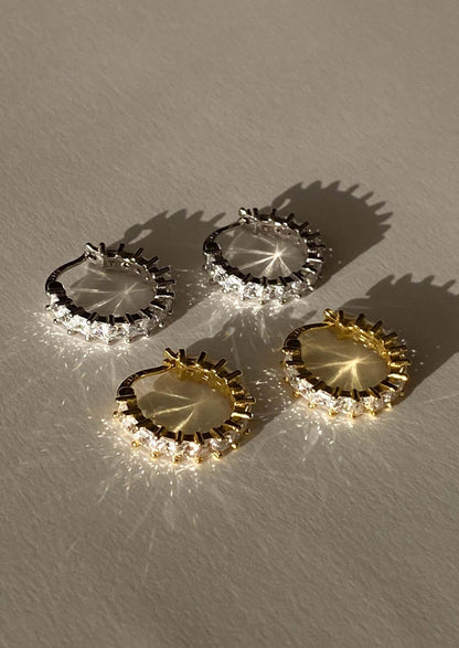 Four pairs of hoop earrings in gold and silver on a textured surface.