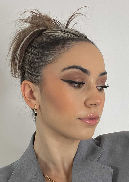 Woman with styled hair and makeup wearing a gray blazer against a plain background