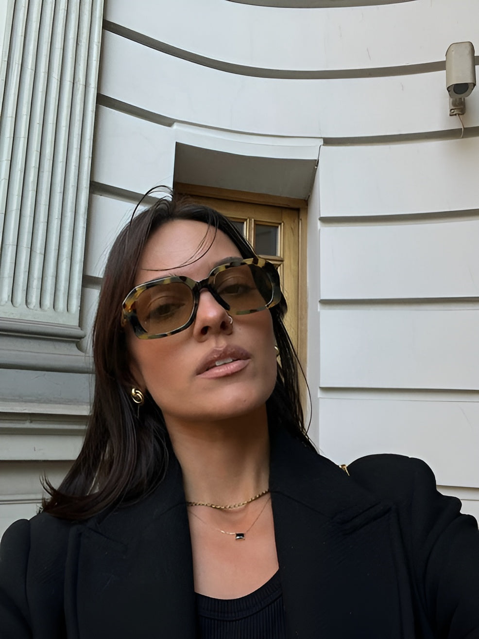 Woman wearing sunglasses and a black outfit standing in front of a house.