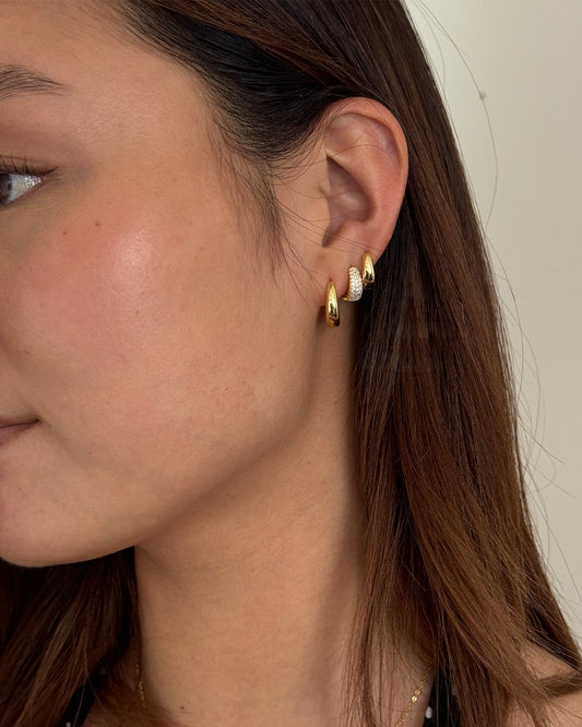 Close-up of a person wearing gold hoop earrings with small diamonds.