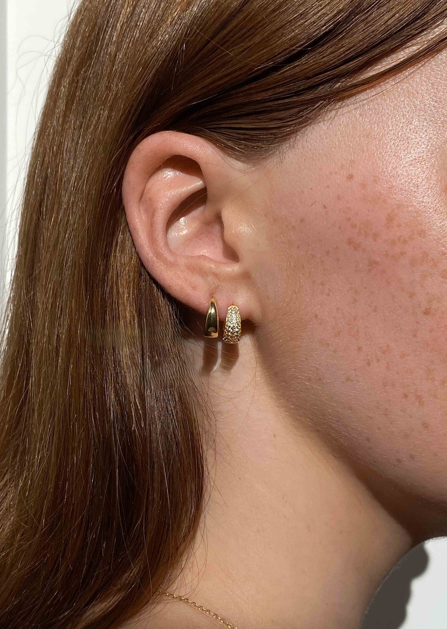 Close-up of a person wearing gold hoop earrings with a neutral background