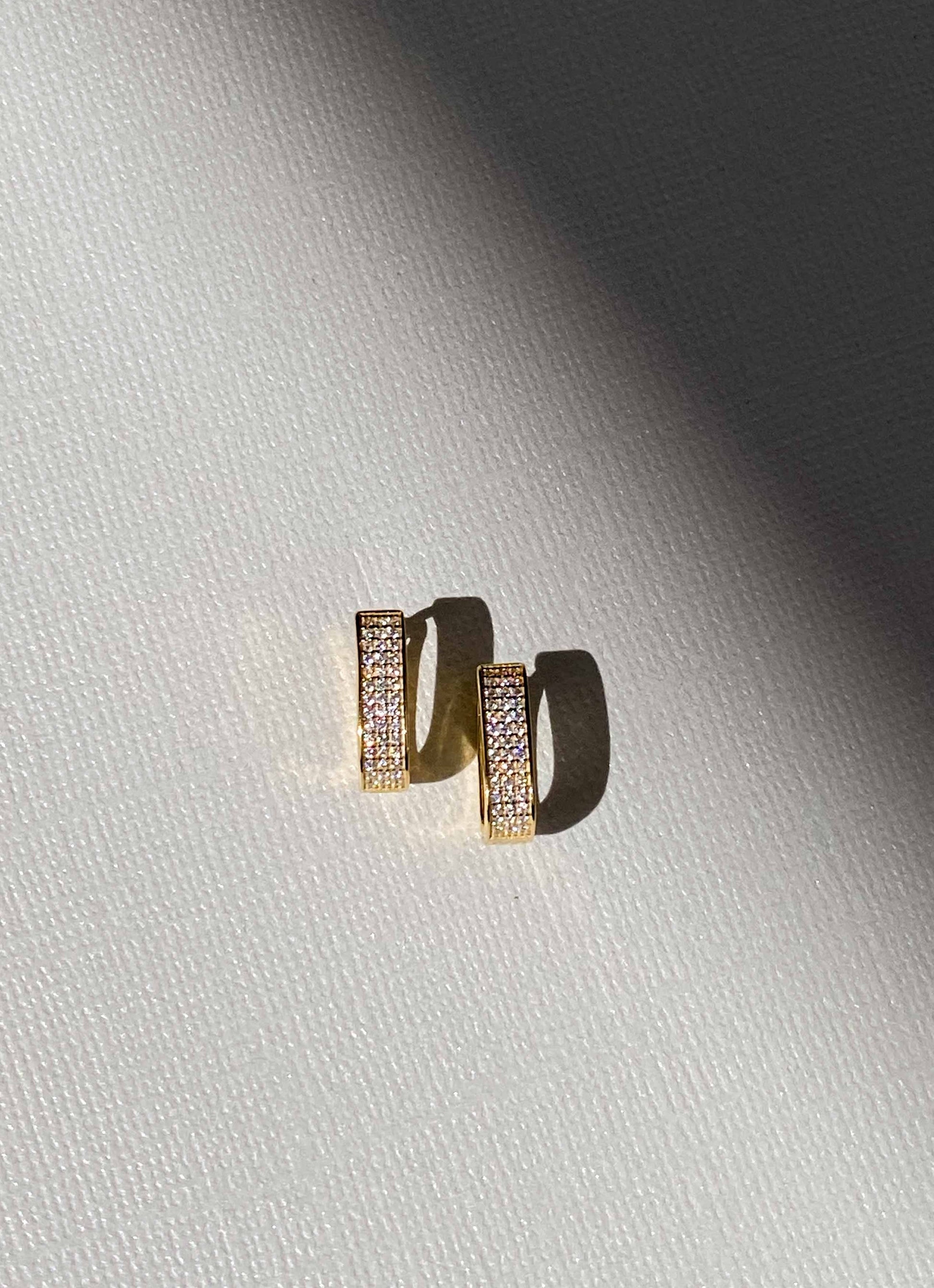 Gold hoop earrings with embedded stones on a light gray background