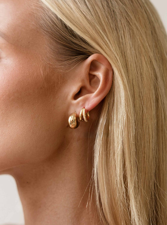Close-up of a person wearing gold hoop earrings with a neutral background
