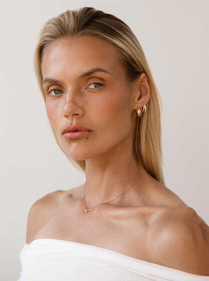 Woman wearing a gold earring and necklace against a plain background