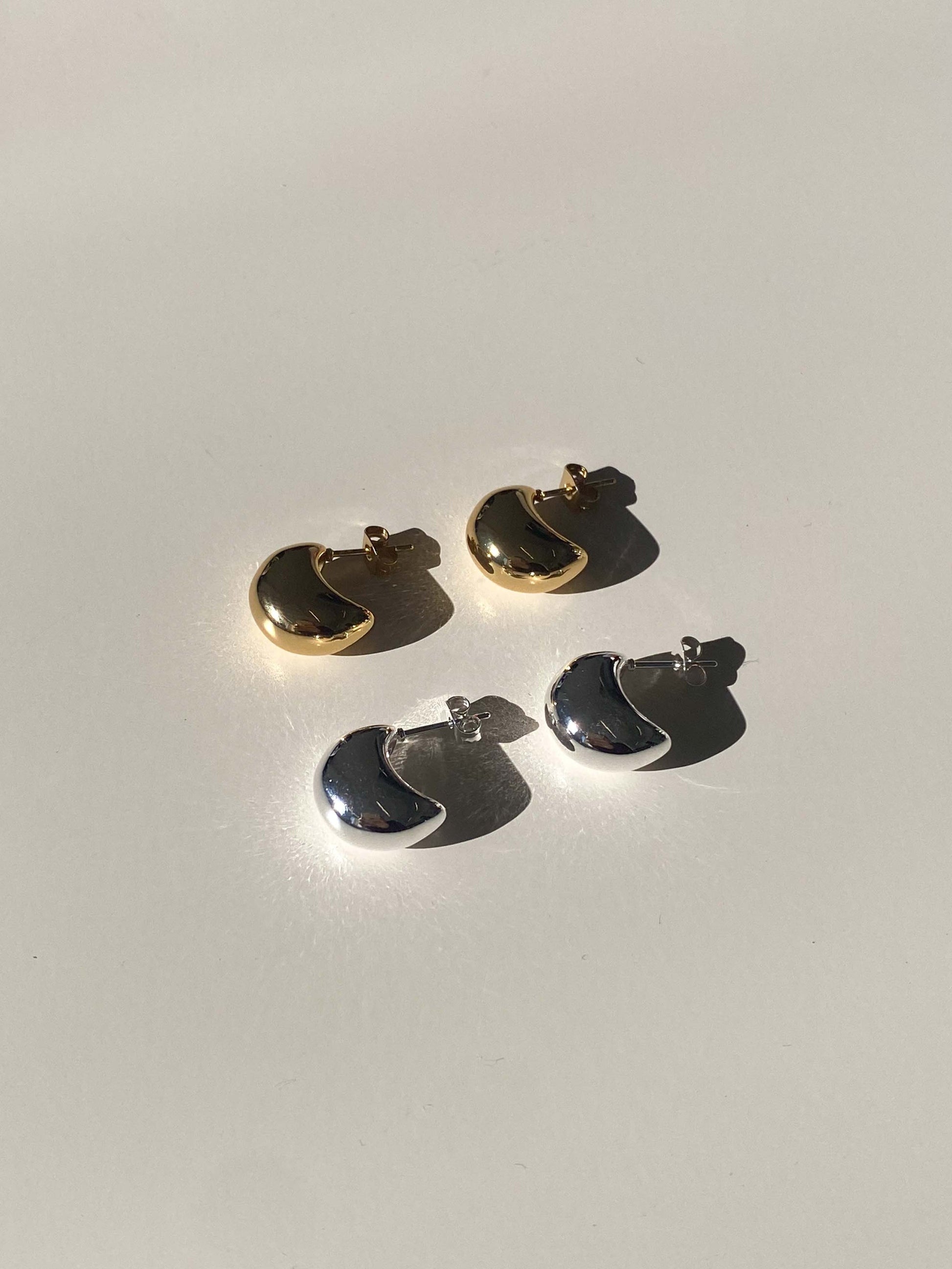 Two pairs of gold and silver earrings on a light gray background