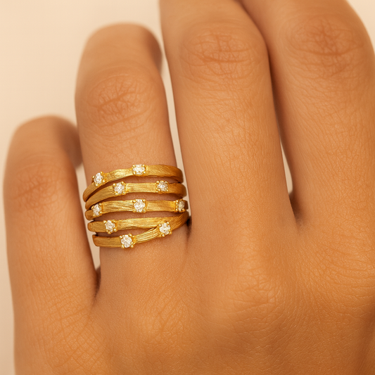 Gold rings with diamond accents on a hand against a beige background