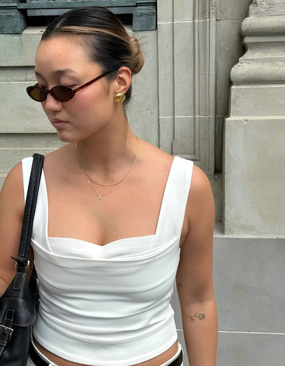 Woman wearing a white top and sunglasses, standing against a stone wall.