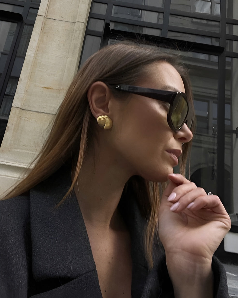 Woman wearing sunglasses and a black coat with a blurred urban background