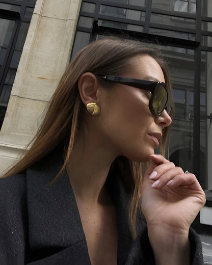 Woman wearing sunglasses and a black coat with a blurred urban background