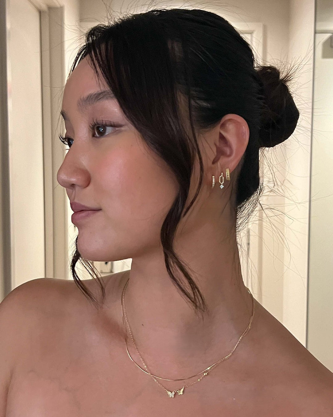 Woman wearing gold earrings and necklace with a neutral background