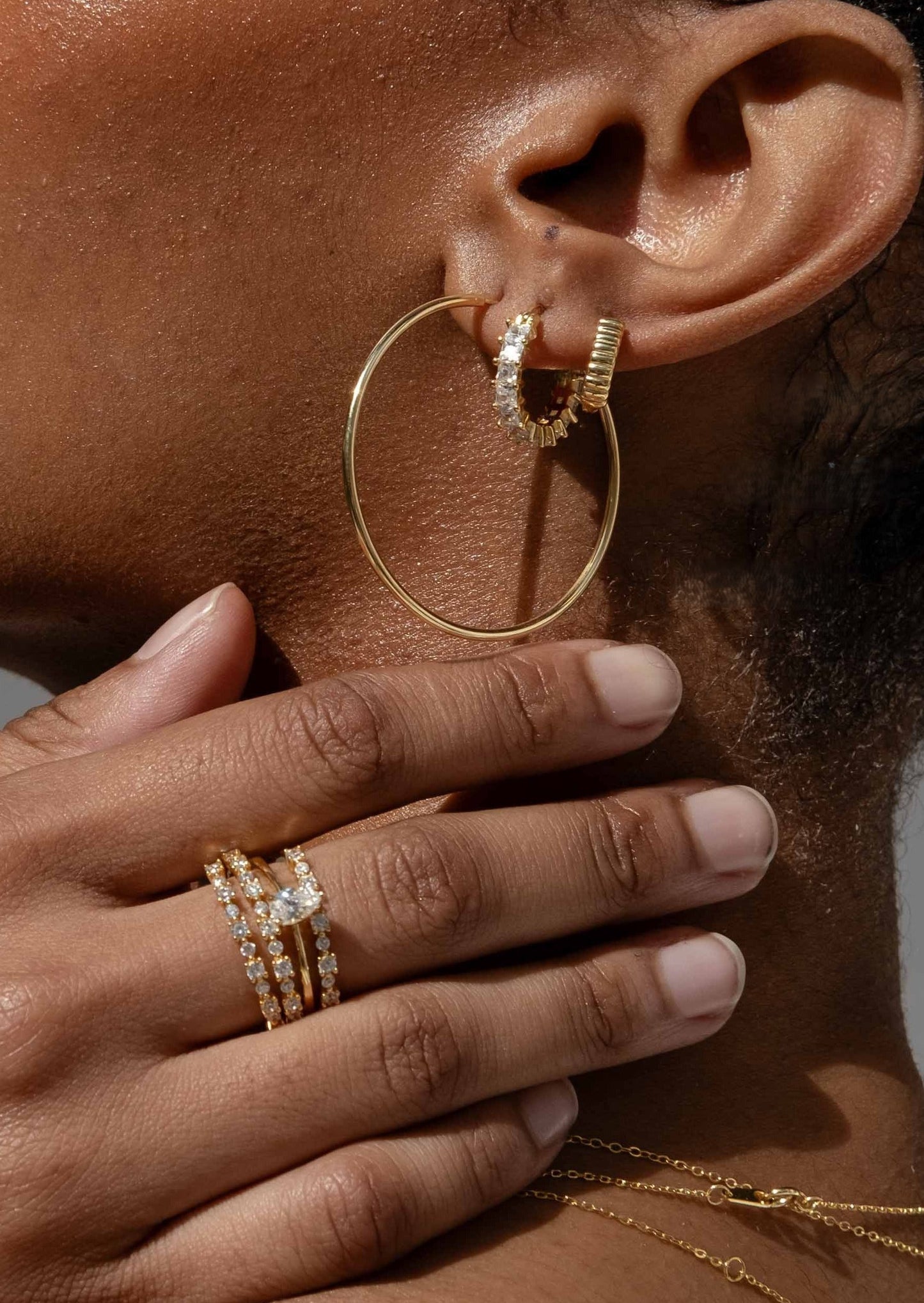 Close-up of an ear with gold hoop earrings and rings, hand touching face