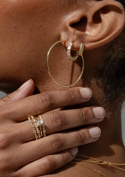 Close-up of an ear with gold hoop earrings and rings, hand touching face