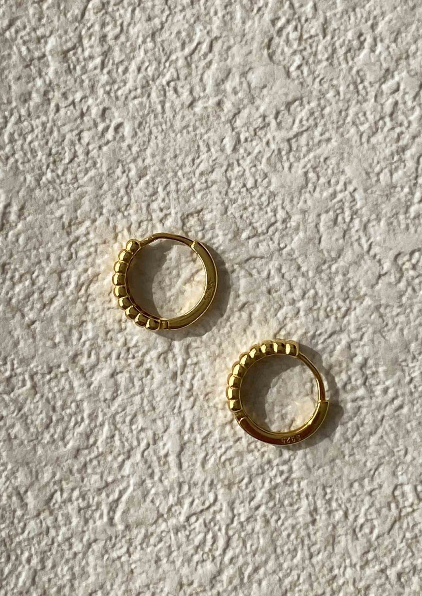 Gold hoop earrings on a textured white surface
