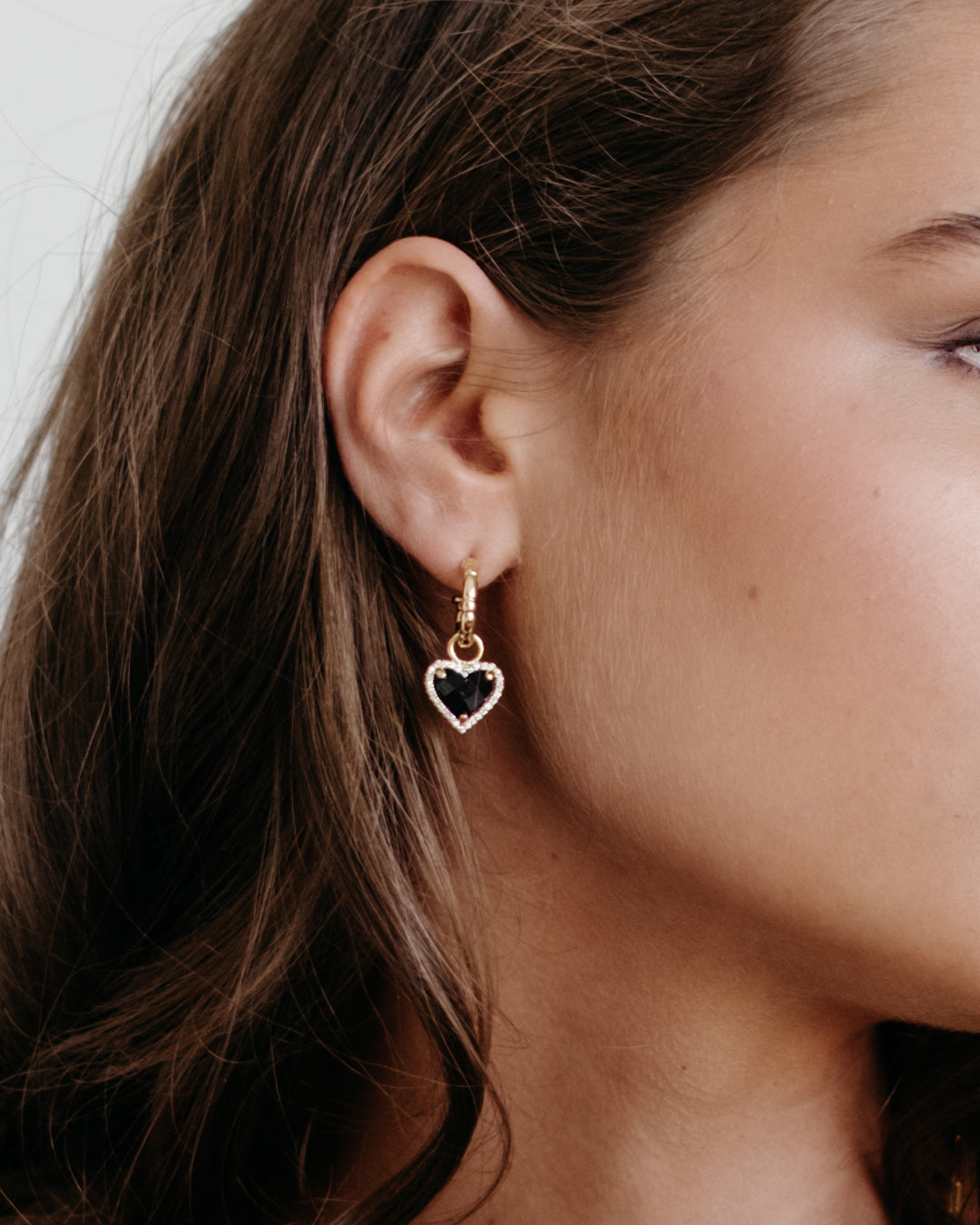 Close-up of a person wearing a heart-shaped earring with a black stone.
