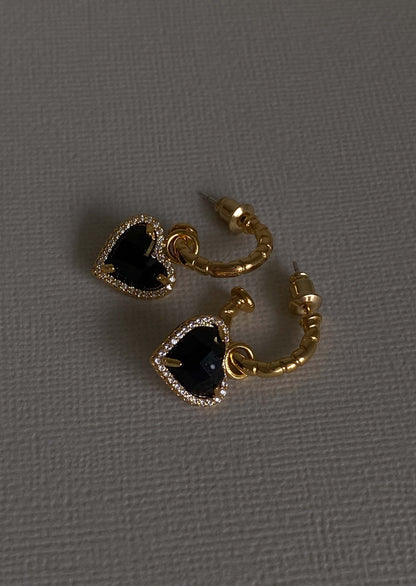 Gold hoop earrings with black gemstones on a gray background