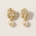 Pair of pearl earrings with gold accents on a beige background