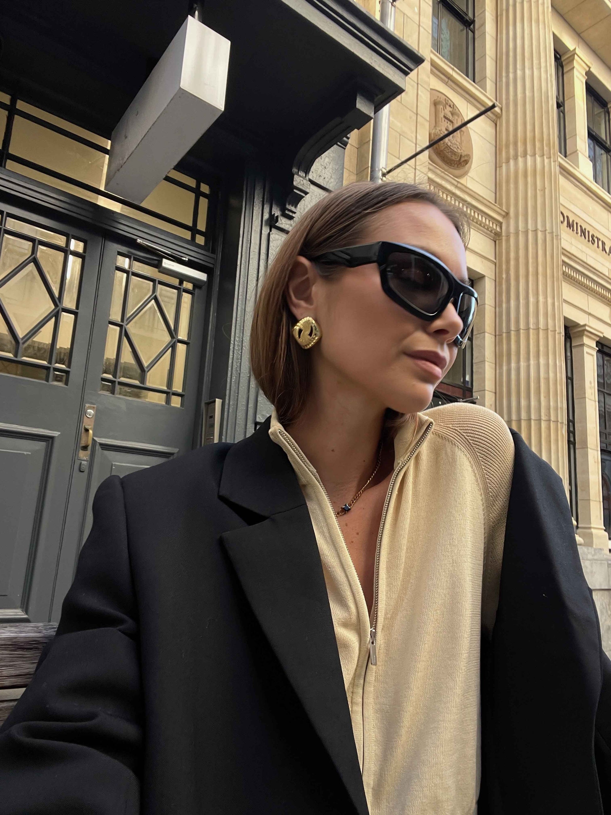 Woman wearing sunglasses and a black coat in front of a building
