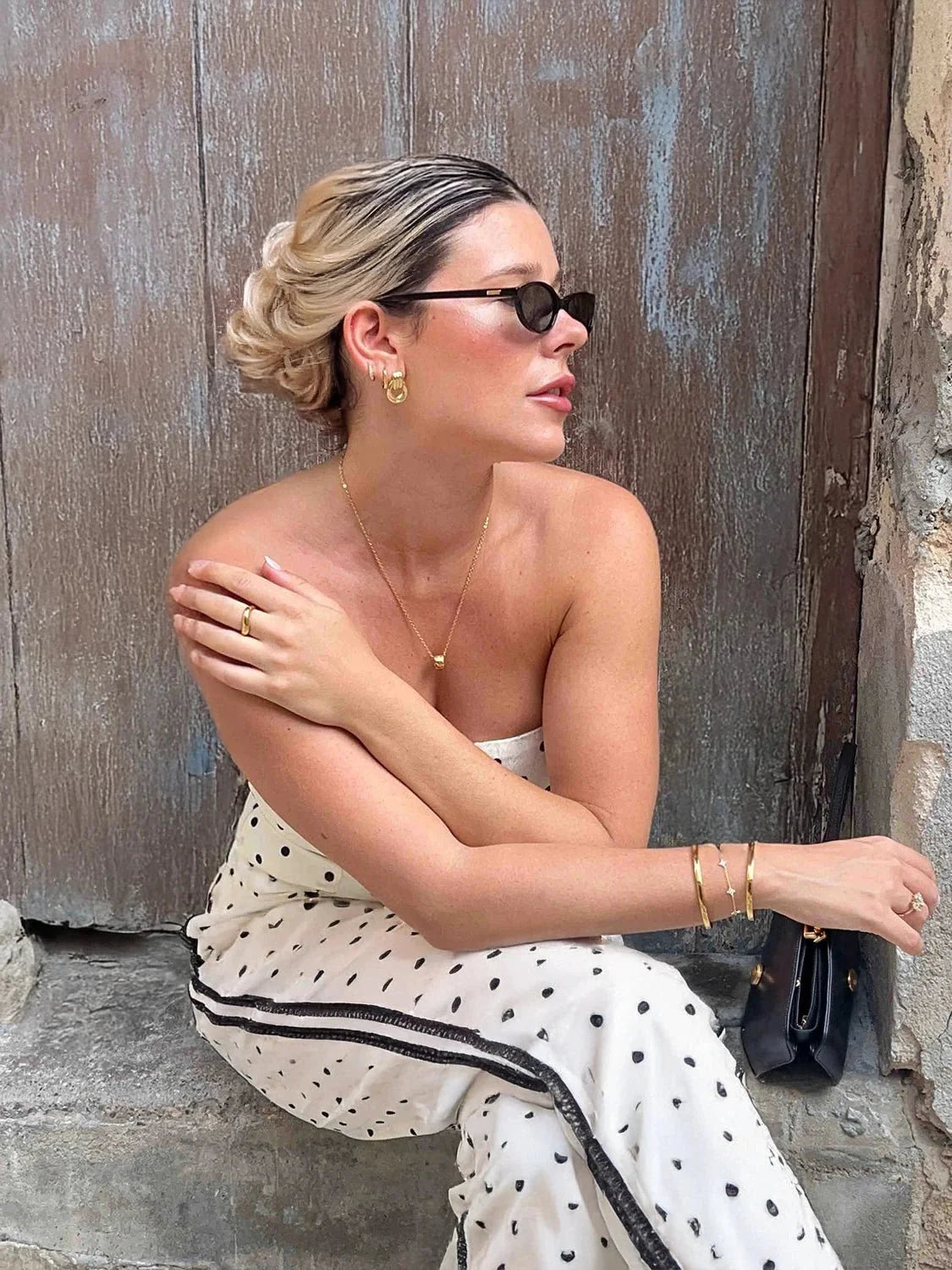 Woman in a polka dot dress sitting against a textured wall.