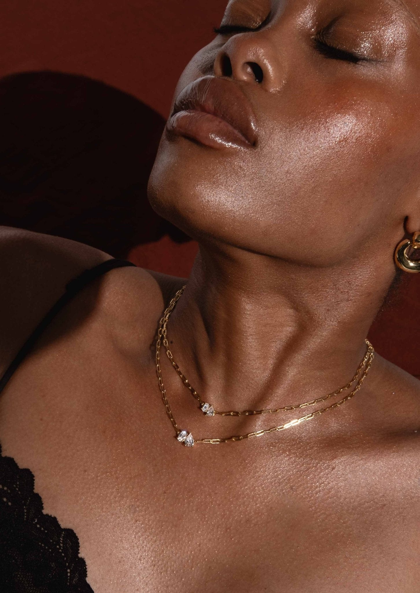 Close-up of a woman wearing layered gold necklaces with diamond pendants, showcasing elegant jewelry against a dark background.