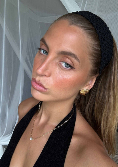 Woman with black headband and halter top, wearing gold earrings and necklace, posing indoors. Fashion, beauty, and accessories.